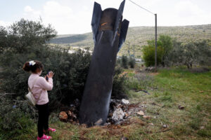 Ένα κορίτσι στέκεται δίπλα στα συντρίμμια ενός πυραύλου που έχει καρφωθεί στο έδαφος, τα οποία βρέθηκαν στο χωριό Κιφλ Χάρις, κοντά στη Ναμπλούς, στη Δυτική Όχθη που βρίσκεται υπό ισραηλινή κατοχή, στις 24 Μαρτίου 2026. REUTERS/Mohammed Torokman