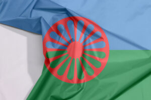 Σημαία από ύφασμα με μοτίβα Ρομά, με πτυχώσεις και λευκούς χώρους, μπλε και πράσινο φόντο που συμβολίζουν τον ουρανό και τη γη, και ένα κόκκινο τσάκρα ή τροχό στο κέντρο. istock